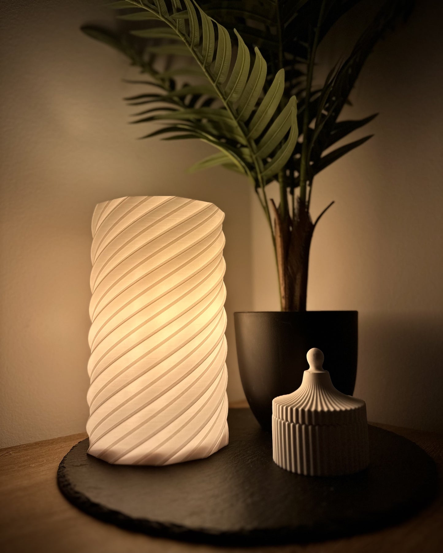 Tischlampe im modernen Design, spiralförmig, warmweiß leuchtend, dimmbar, zusammen mit Pflanze und Aufbewahrungsbehälter