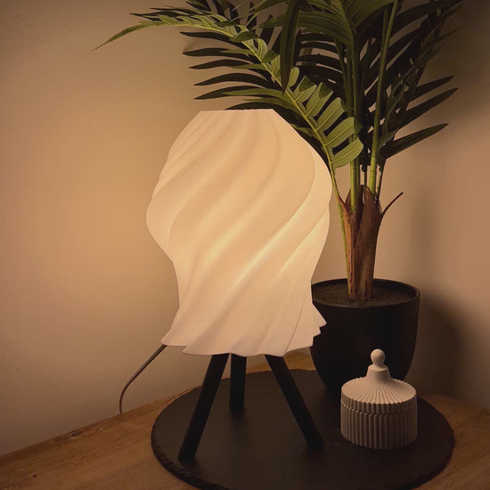 Moderne, dimmbare Lampe mit geschwungenem Schirm und Dreibeinfuß, begleitet von einer stilvollen Dose