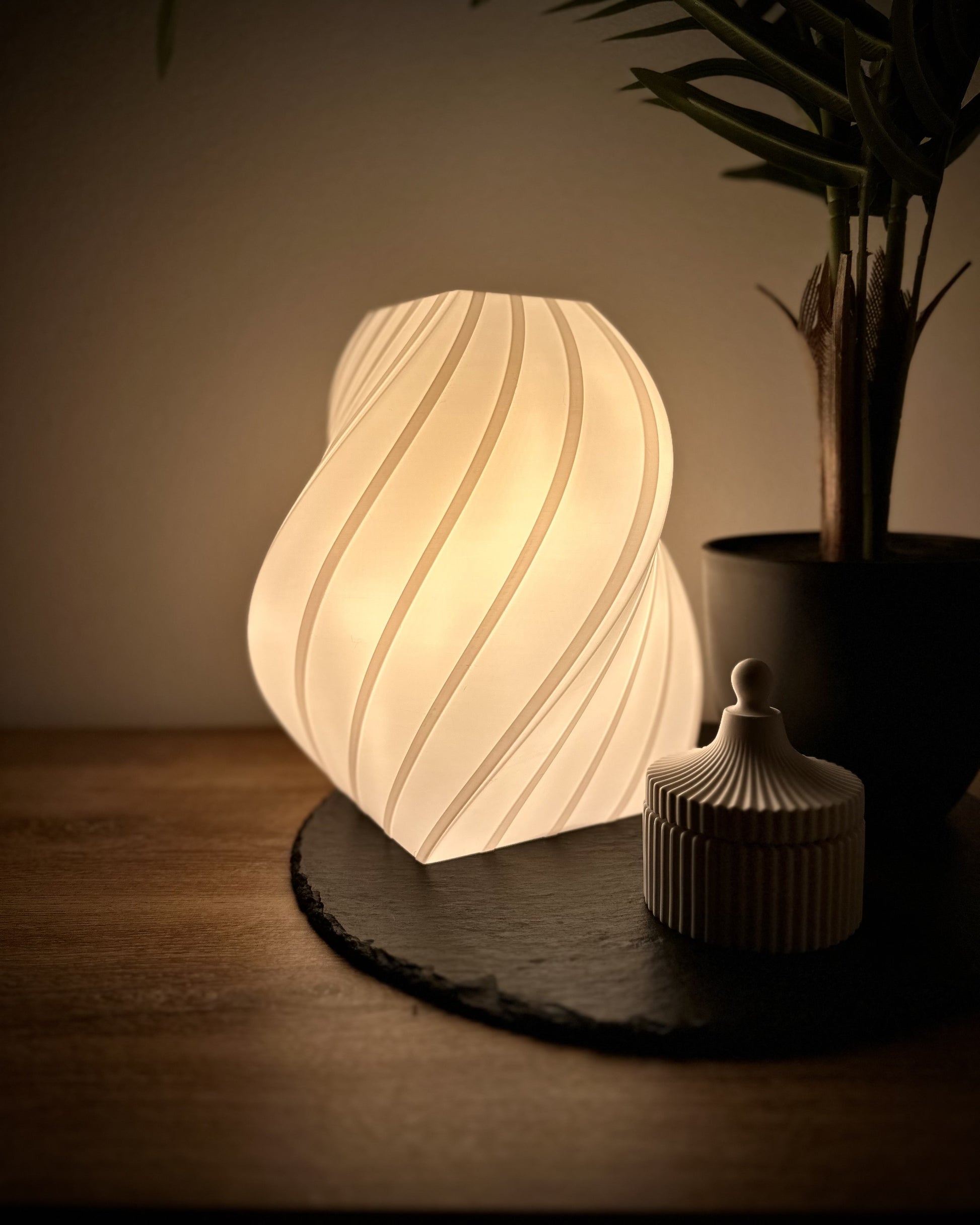 Moderne Tischlampe mit geschwungenem Design, warmweiße Beleuchtung, dimmbar, arrangiert mit Pflanze und Dose