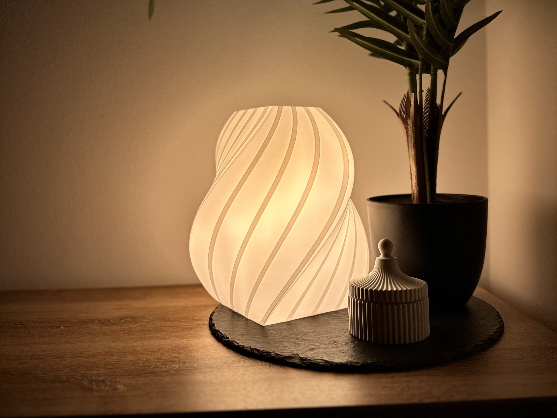 Warmweiße, dimmbare Tischlampe mit elegant geschwungenem Schirm, dekoriert mit Pflanze und Deko-Dose