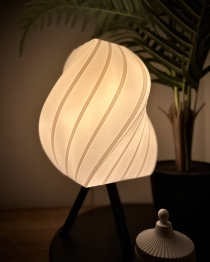 Dimmbare Lampe mit geschwungenem, bauchigem Schirm und warmweißem Licht, neben Pflanze und dekorativer Dose