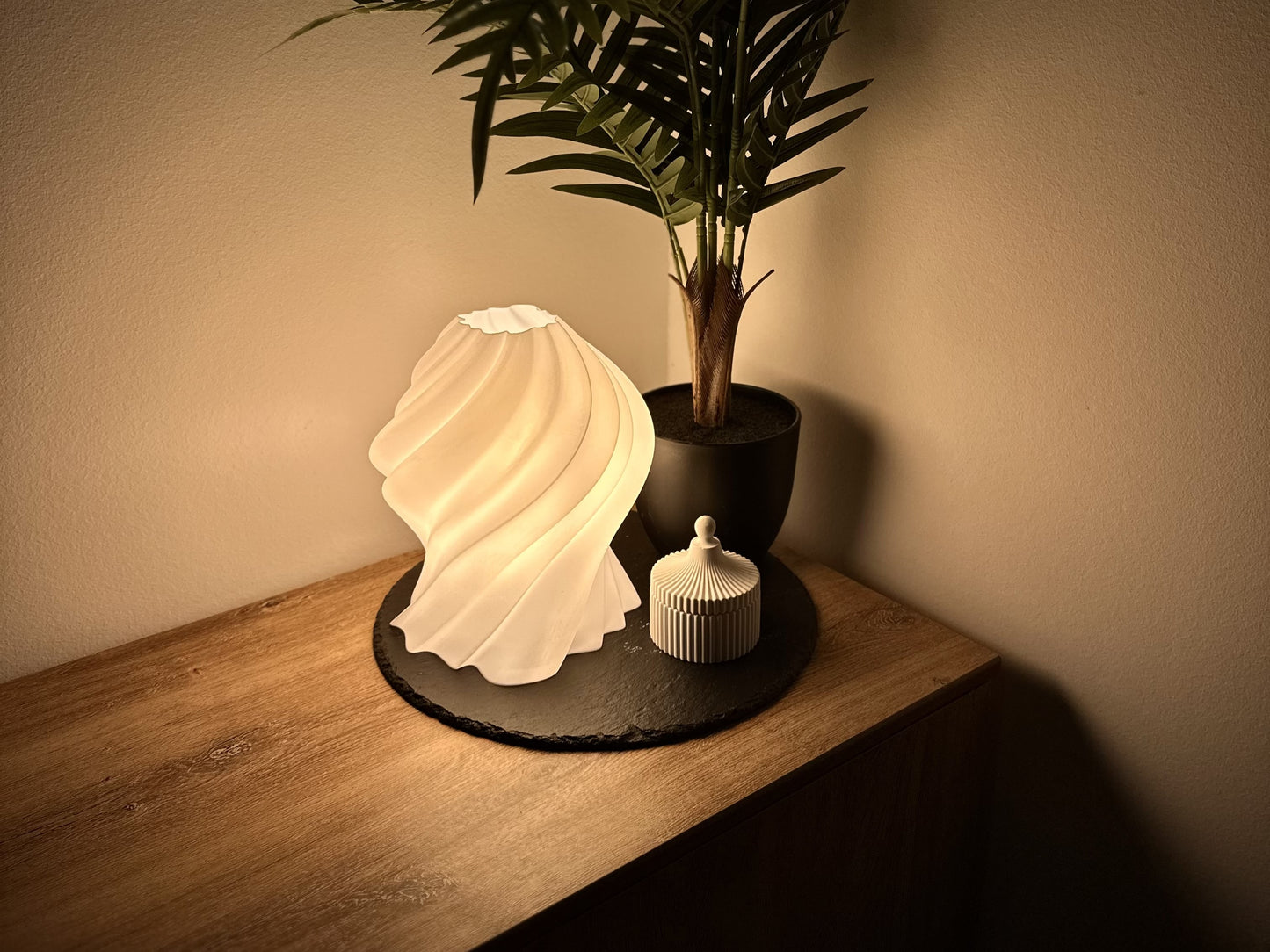 Elegante, dimmbare Lampe mit geschwungenem Schirm, neben einer modernen Dekodose