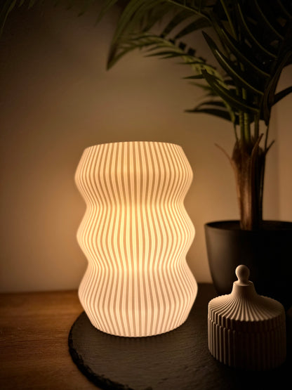 Moderne Dimmbare Tischlampe mit wellenförmigem Schirm, warmweißes licht, neben Pflanze und Deko