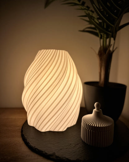 Moderne Designer-Tischlampe mit elegantem Spiralmuster-Schirm, warmweiß, dimmbar, kombiniert mit Pflanze und Dose